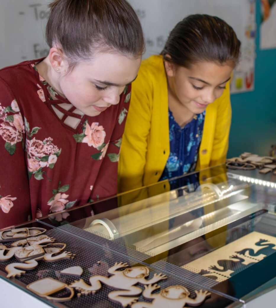 Two young students looking into the glass top of the Glowforge